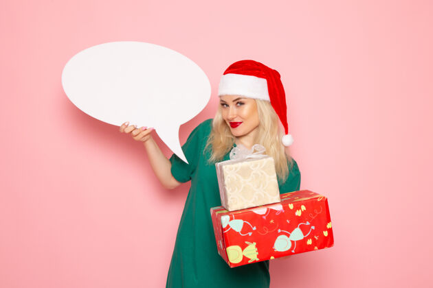 女人正面图年轻女性手持圣诞礼物和白色标志在粉色墙上的女性礼物雪地彩照新年假期快乐购物圣诞节