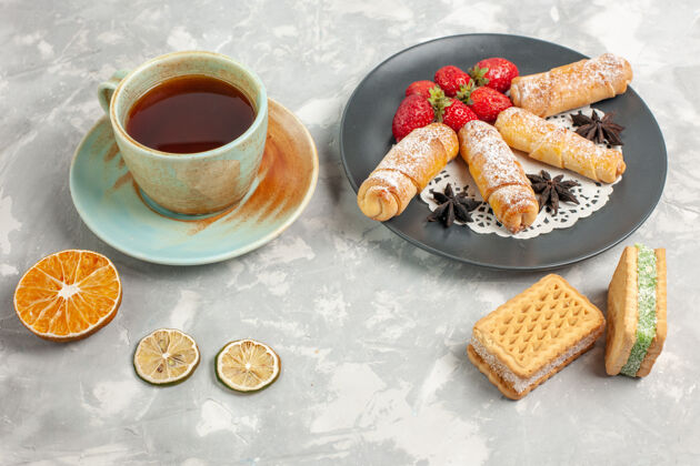 茶白色书桌上的草莓和一杯茶糖粉卷的正视图蛋糕糕点草莓