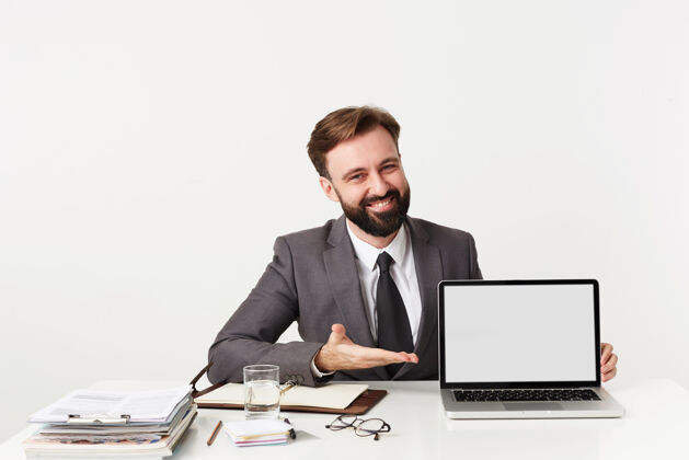 积极年轻快乐的留着黑胡子 发型时髦的男性 在办公室开会 在笔记本电脑上演示一些东西 穿着灰色西装 打着白色的领带笔记本电脑男士屏风