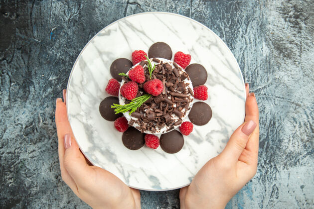 椭圆形俯视图巧克力芝士蛋糕放在椭圆形盘子里 女人手放在灰色的表面上草莓巧克力芝士蛋糕盘子