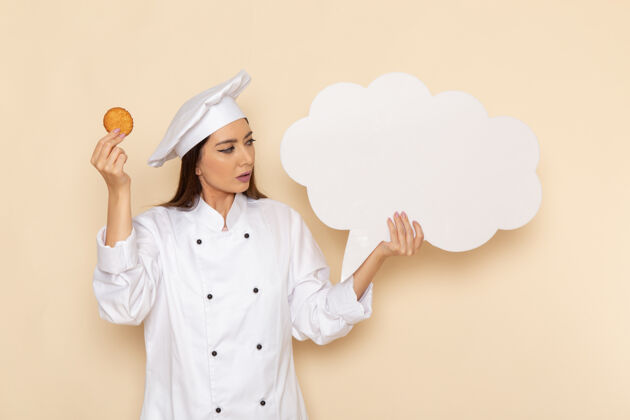 专业身穿白色厨师服的年轻女厨师手持饼干 在浅白的墙上挂着白色的招牌工作女性快乐