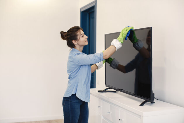 工作在家工作的家庭主妇穿蓝色衬衫的女士清洁电视的女士工人清洁房间
