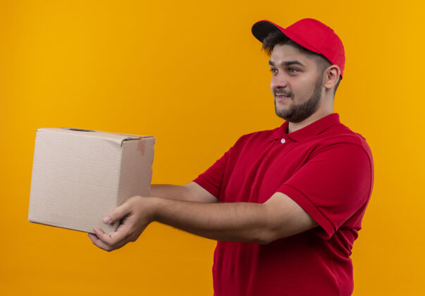 站立年轻的送货员身着红色制服 戴着帽子 微笑着向顾客赠送礼盒包装制服送货帽子