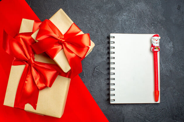 毛巾圣诞背景与美丽的礼物蝴蝶结形缎带上的红毛巾和笔记本与笔在黑暗的背景钢笔圣诞节蝴蝶结
