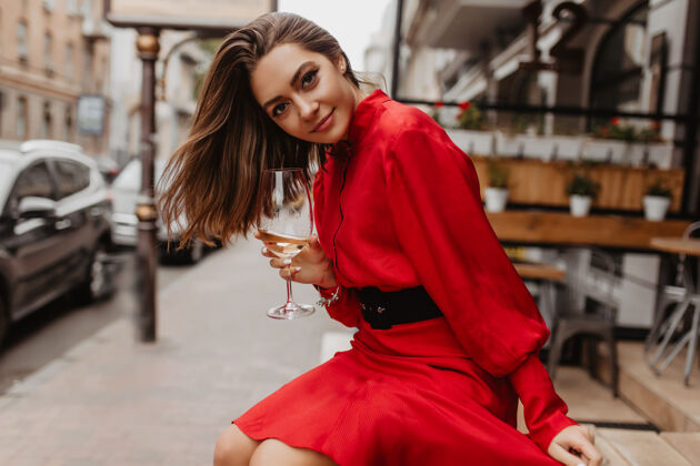 城市心满意足 甜美的女孩温柔地笑着红色的连衣裙为摆着酒杯的女士的装束增添了光彩腰带街道香槟
