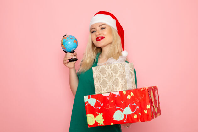 圣诞节正面图年轻女性手持地球仪和圣诞礼物在粉色墙上照片女性圣诞节新年彩色假期风景年轻女性女人