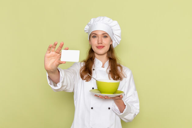 人身着白色厨师服的女厨师正面图 绿色墙壁上有盘子和卡片衣服西装淋浴帽