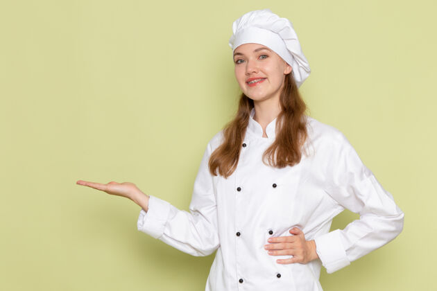 专业身着白色厨师服的女厨师在绿色墙壁上微笑着摆姿势食物前面姿势