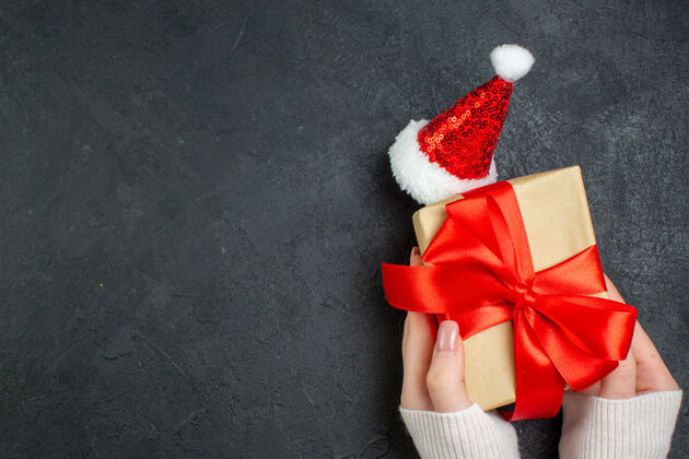蝴蝶结手持精美礼物的俯视图 黑色背景下的圣诞老人帽子旁边有蝴蝶结状的缎带圣诞老人风车视图