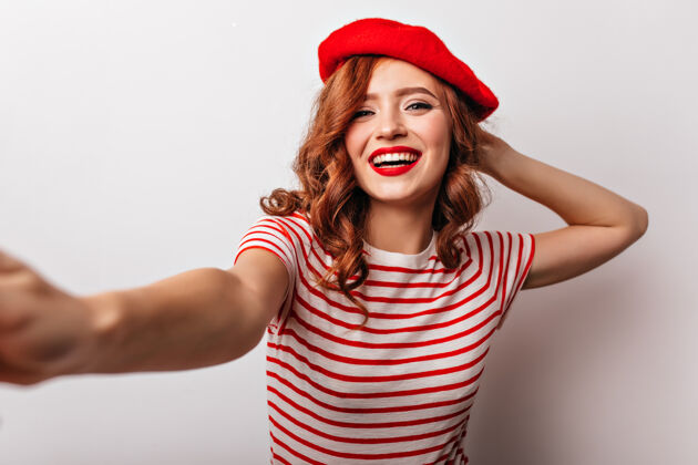 头发穿着红色贝雷帽的迷人的欧洲女孩笑着积极的法国年轻女子自拍Swoosh波浪发配饰