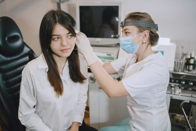 健康医务室的女病人戴着医用口罩的医生医生检查女人的耳朵疾病耳朵医生