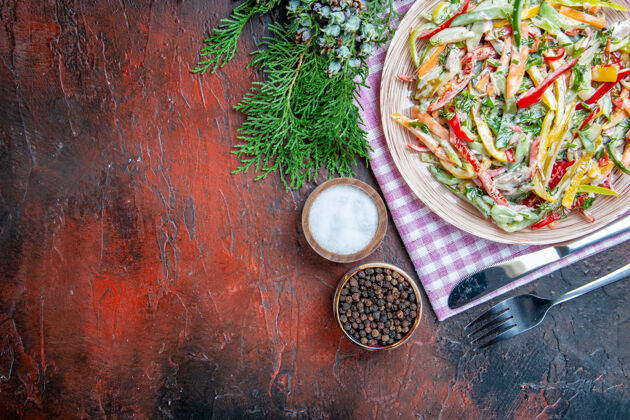 叉子顶视图蔬菜沙拉放在餐盘上 餐叉和刀子上 盐和黑胡椒放在深红色的桌子上 自由空间盐胡椒粉桌布