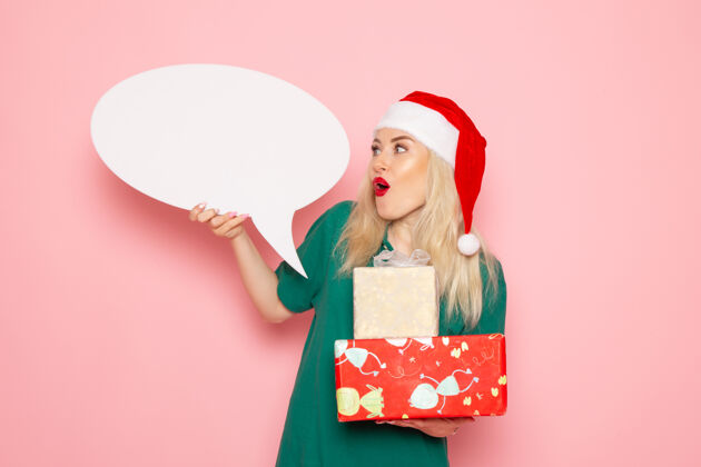 颜色正面图年轻女性手持圣诞礼物和白色标志在粉色墙上的女性礼物雪地彩照新年假期购物年轻女性女人