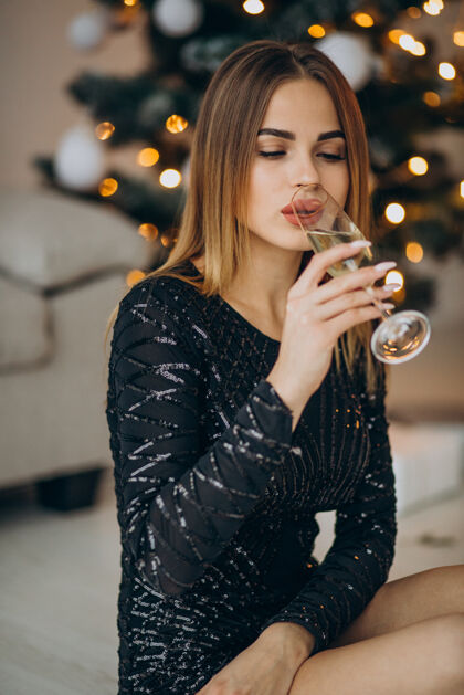 时尚年轻女子在圣诞树旁喝香槟新年轻女人快乐