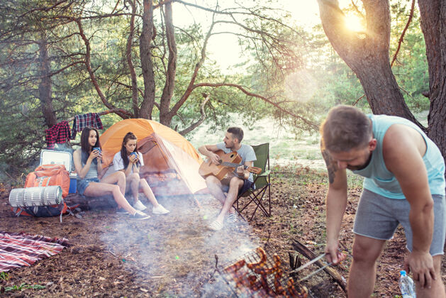 篝火聚会 男女在森林露营露营坐着烹饪