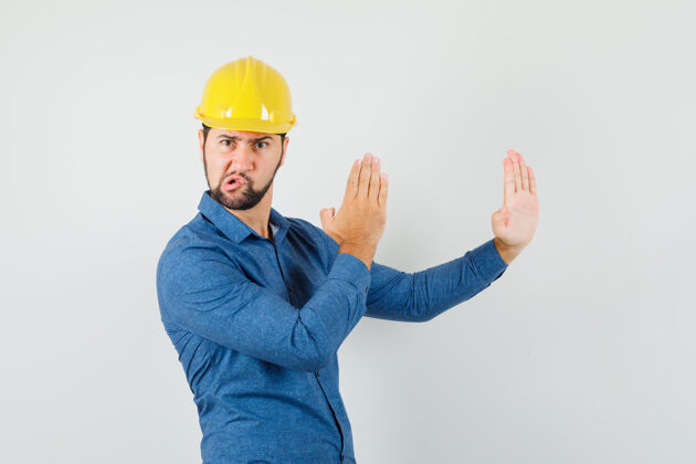 工程师一个年轻的工人穿着衬衫 戴着头盔展示着空手道砍人的动作 看上去很生气沟通头脑风暴专业