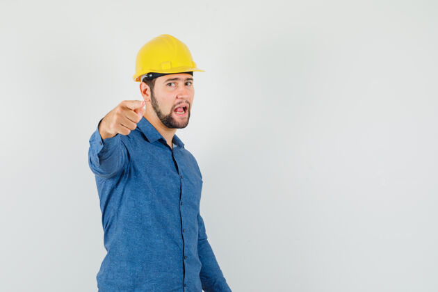 工程师穿着衬衫 戴着头盔的年轻工人指着摄像机 看上去很自信劳动职业自信