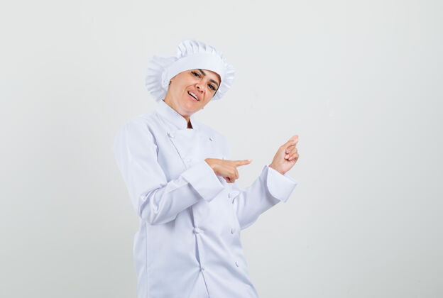 制服穿着白色制服的女厨师指着别处 看上去很高兴女性柜台专业