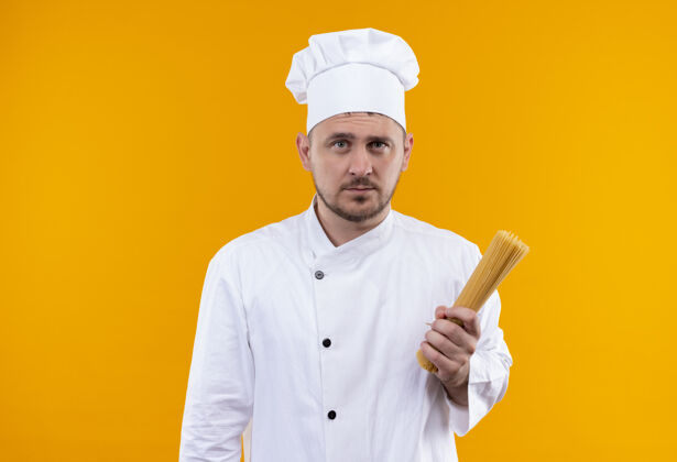 厨师年轻帅气的厨师穿着厨师制服 手里拿着意大利面 看起来孤立在橙色的空间里拿着意大利面橙色