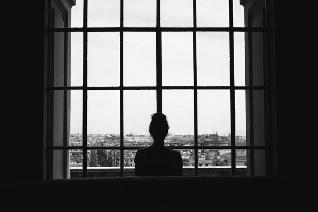 玻璃黑白照片 一个孤独的女人站在窗户前看着建筑物年轻人里面
