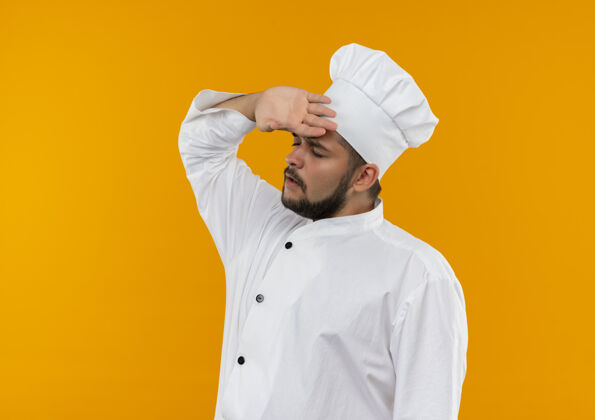 前额穿着厨师制服的年轻男厨师 紧张地把手放在额头上 闭着眼睛 孤立地站在橙色的空间里制服眼睛复制