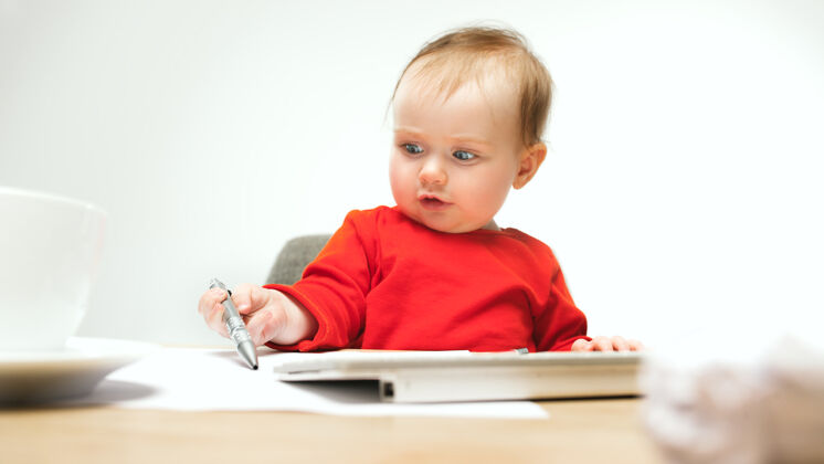 桌子快乐的小女婴坐在一个白色的工作室里 手里拿着现代电脑或笔记本电脑的笔和键盘孩子屏幕学习