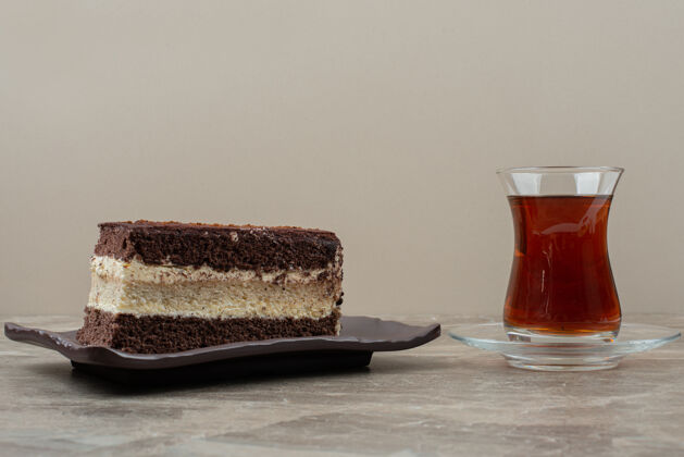 蛋糕在大理石桌上放一片巧克力蛋糕和一杯茶甜点茶盘子