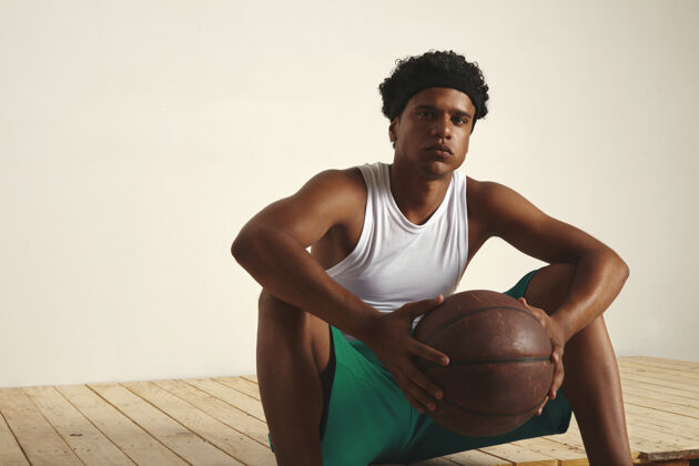 坐着一个非常疲倦的篮球运动员坐在地板上 手里拿着球休息自信篮子现代