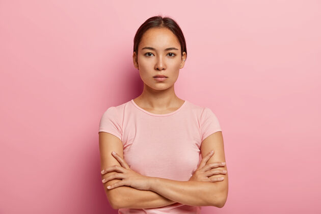 皮肤严肃的韩国女人头像表情镇定 双臂合十 皮肤健康清新 身穿玫瑰色t恤 站在室内美丽的亚洲女孩有自信的目光外观自信手臂