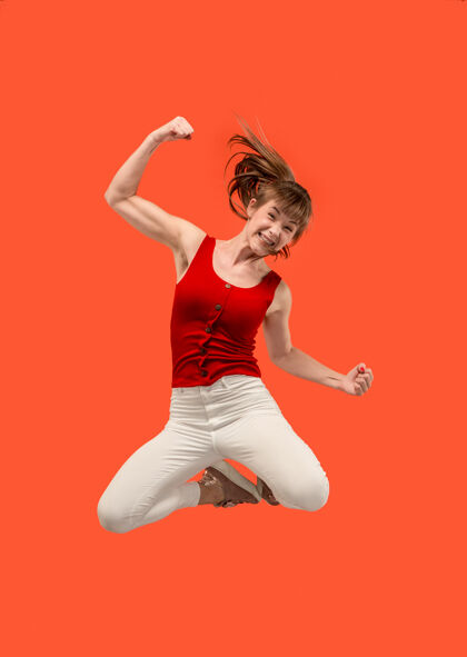 胜利在移动的自由相当快乐的年轻女子跳跃和对橙色的手势半空中拍摄舞蹈活动时尚
