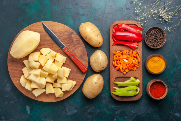 盘子顶视图：深蓝色背景上的新鲜土豆片 调味料和辣椒片小吃饮食美味