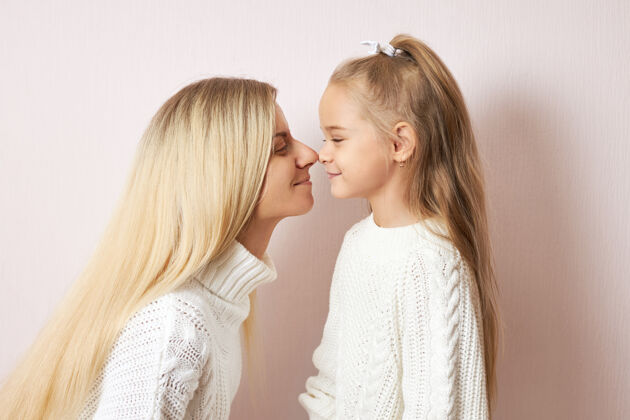 童年一头金色长发的快乐年轻女性将亲吻她迷人的小女儿 鼻尖贴在一起爱 家庭 世代和关系鼻子幸福肖像