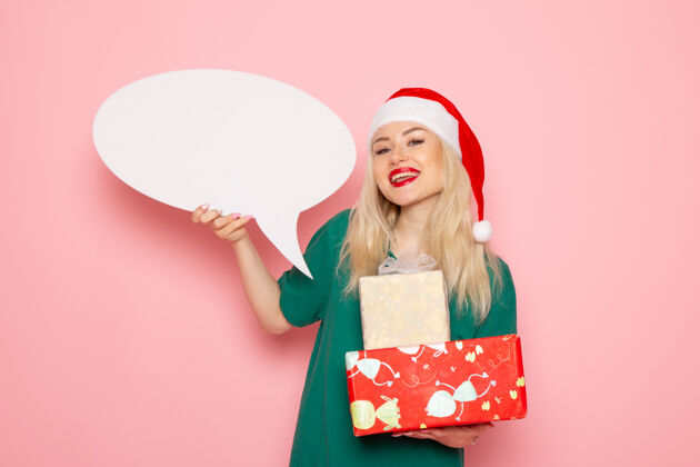 美丽正面图年轻女性手持圣诞礼物和白色标志在粉色墙上情感女性礼物雪地彩照新年假期情感购物年轻的女人