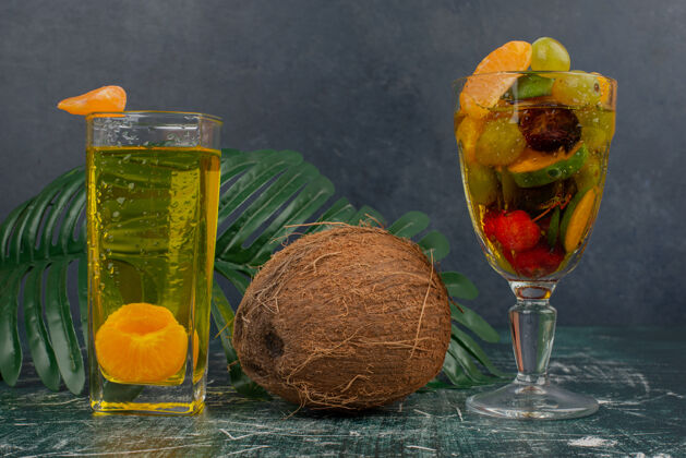 橘子大理石桌上放着一杯混合水果 果汁和椰子罐子盘子水果