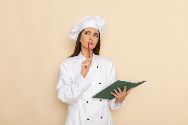 工作身穿白色厨师服的年轻女厨师手持抄写本 在浅白的墙上思考女性年轻专业