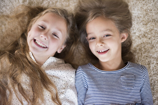 肖像可爱的妹妹在蓬松的地毯上玩得很开心友谊躺着舒适