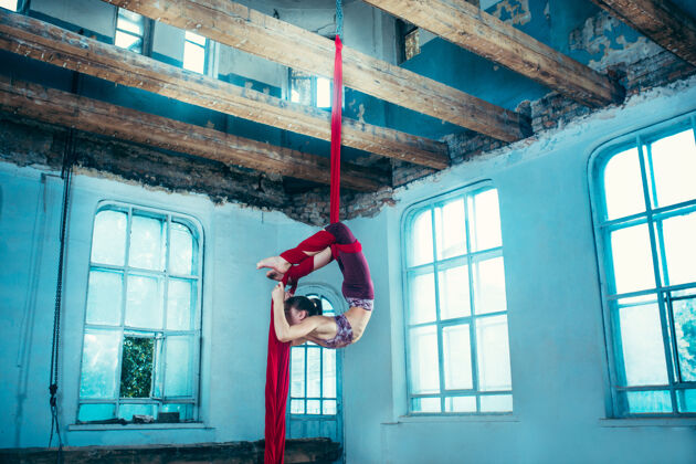 表演优雅的体操运动员在蓝色的老阁楼上用红色织物进行空中练习舞蹈技能丝绸