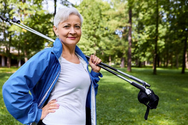 退休60多岁自信美丽的高加索女性退休老人享受退休生活的画面 肩上扛着登山杖 准备让北欧人在户外散步 手放在腰上北欧人散步服装