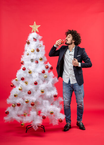 庆祝圣诞节庆典上 留着胡子的年轻人站在红地毯上的圣诞树旁喝酒站着男人打扮