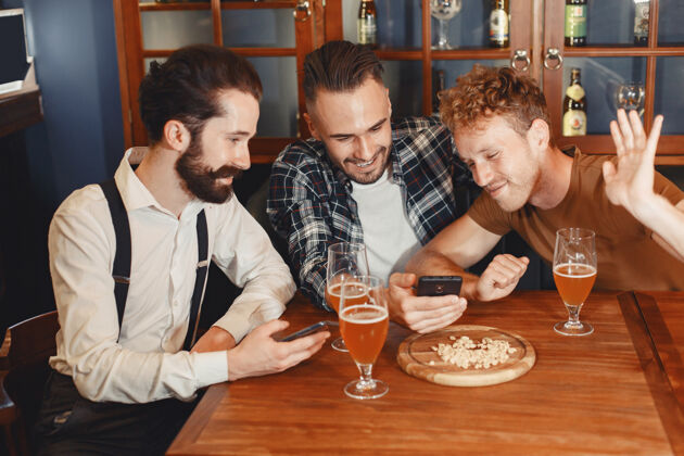 交谈和最好的朋友见面三个穿着休闲服的快乐的年轻人一起坐在酒吧里聊天喝啤酒休闲快乐桌子
