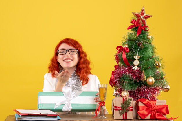 树前视图：女医生拿着圣诞礼物和黄色背景上的圣诞树坐着礼物庆祝快乐