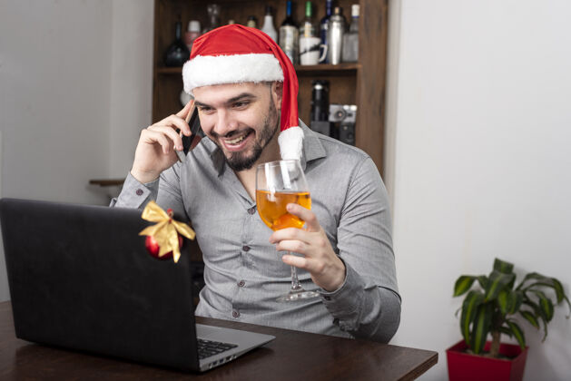 快乐特写镜头一个西班牙裔男子戴着圣诞老人的帽子 享受他的酒和电话交谈电话葡萄酒讲话