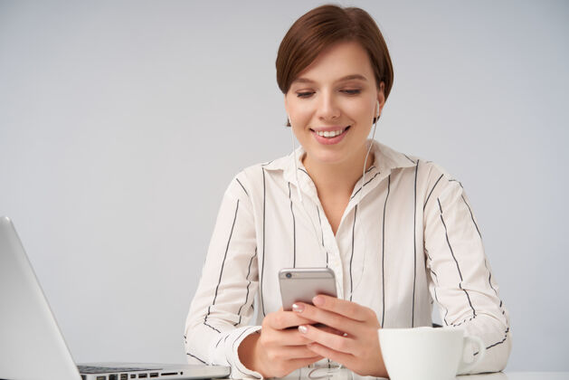 衣服一位年轻的棕色头发的女性 留着一头时髦的短发 坐在白色的椅子上 手举着手机 脸上洋溢着笑容女商人女士女性