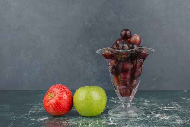 有机湿苹果和一杯黑葡萄放在大理石桌上完整的湿的天然