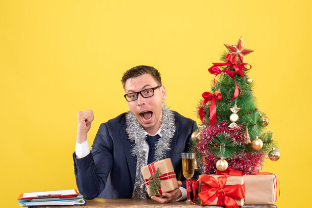 男人戴眼镜的快乐男人坐在圣诞树旁的桌子前 黄色的礼物圣诞快乐的男人快乐