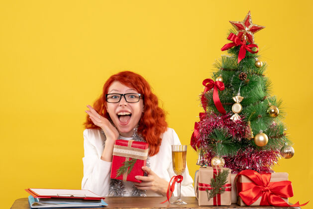 人前视图：女医生坐在桌子后面 黄色背景上有圣诞礼物节日情感快乐