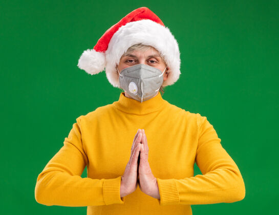 圣诞节高兴的老妇人戴着圣诞帽 戴着医用口罩 手牵着手 隔离在绿色背景上 留有复印空间抱着新手