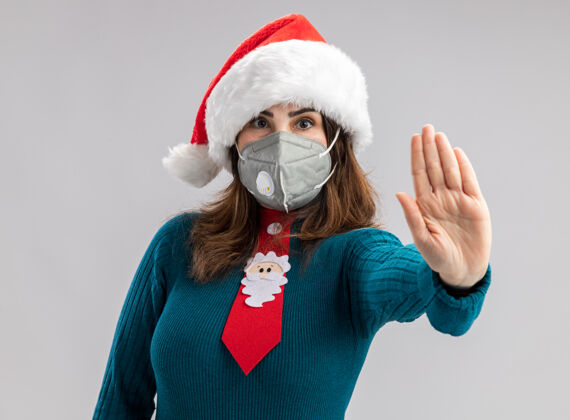 医疗自信的成年白人妇女戴着圣诞帽 打着圣诞领带 戴着医用面罩 示意停车手势新停止空间