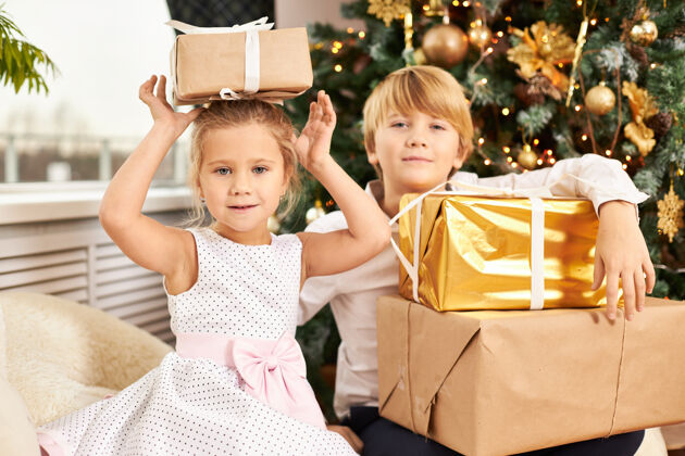 妹妹两个可爱的欧洲儿童兄弟姐妹在圣诞树前合影的照片英俊的少年和他可爱的妹妹一起打开新年礼物 妹妹头上戴着盒子幸福童年传统