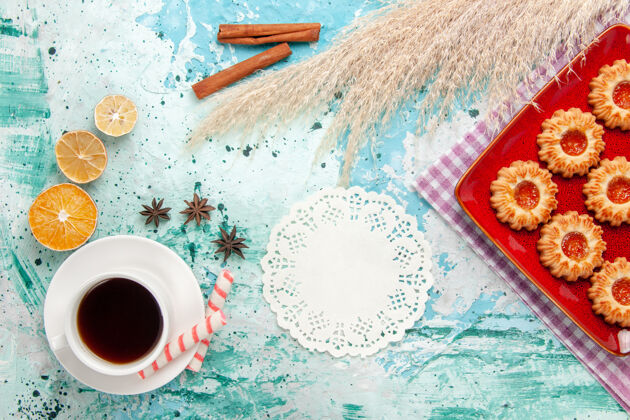 糖顶视图糖饼干在红色盘子里 蓝色背景上有一杯茶热的液体早餐